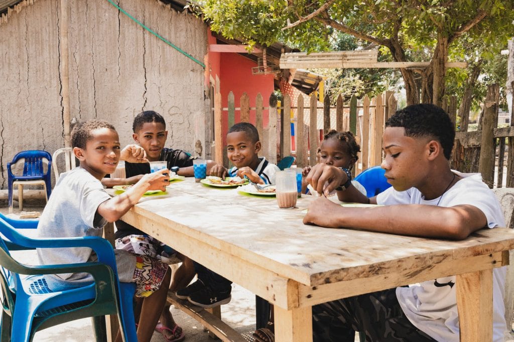 alt="Jungen sitzen an einem Tisch und essen. Sie freuen sich über das Essen und sind dankbar genug davon zu haben. Welthungertag 2024, Compassion Deutschland"