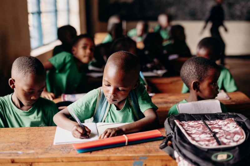 alt="Ein Tag im Compassion Kinderzentrum in Ruanda. Kinder im kinderzentrum mit Stift und Schreibblock am lernen."