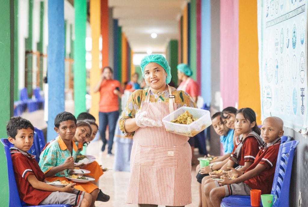 alt="Kochen aus Leidenschaft, Köchin mit Essen in der Hand, Compassion Deutschland"