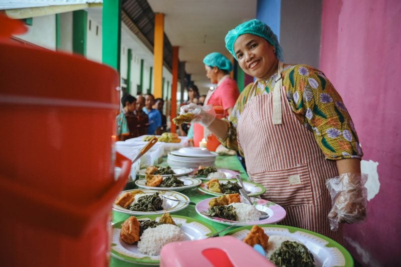 alt="Kochen aus Leidenschaft, Köchin mit Essen auf Tellern, Compassion Deutschland"