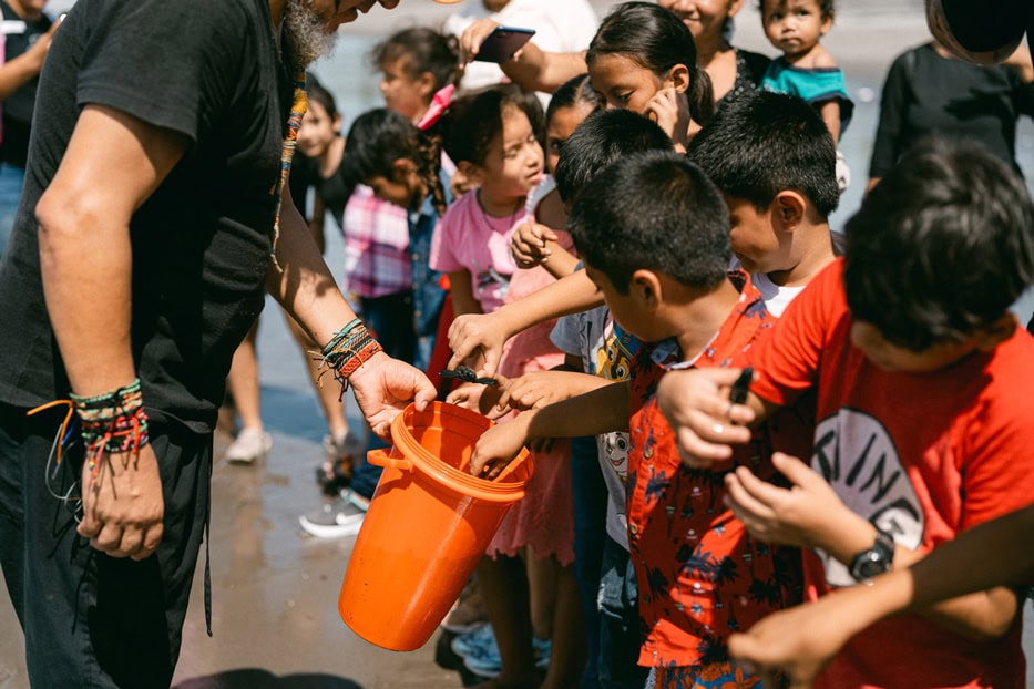 alt="Kinder schützen Meeresschildkröten, Ruben, El Salvador, Kinder stehen in einer Reihe und nehmen Meeresschildkröten aus einem Plastikeimer, Compassion Deutschland"