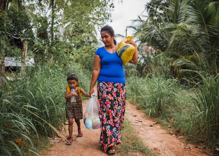 alt="Kampf gegen den Hunger, Mutter mit Kind und Lebensmitteltüten auf einem Weg in Bangladesch, Compassion Deutschland"