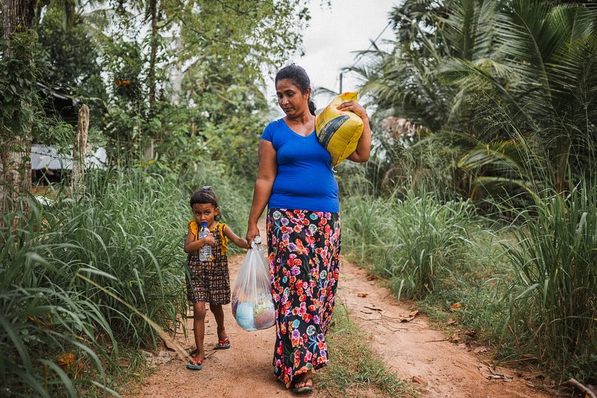 alt="Kampf gegen den Hunger, Mutter mit Kind und Lebensmitteltüten auf einem Weg in Bangladesch, Compassion Deutschland"