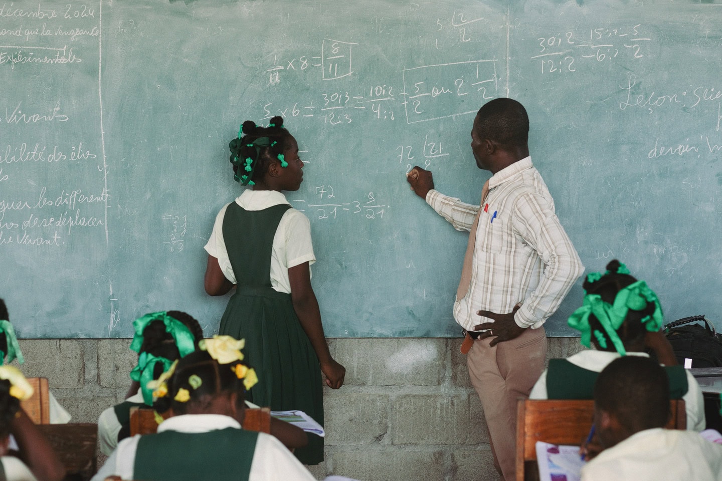 alt="Zum Neuanfang gezwungen, Carolie und Laurie in Haiti, Laurie steht an einer Tafel in der Schule und rechnet, Compassion Kinderzentrum, Compassion Deutschland"